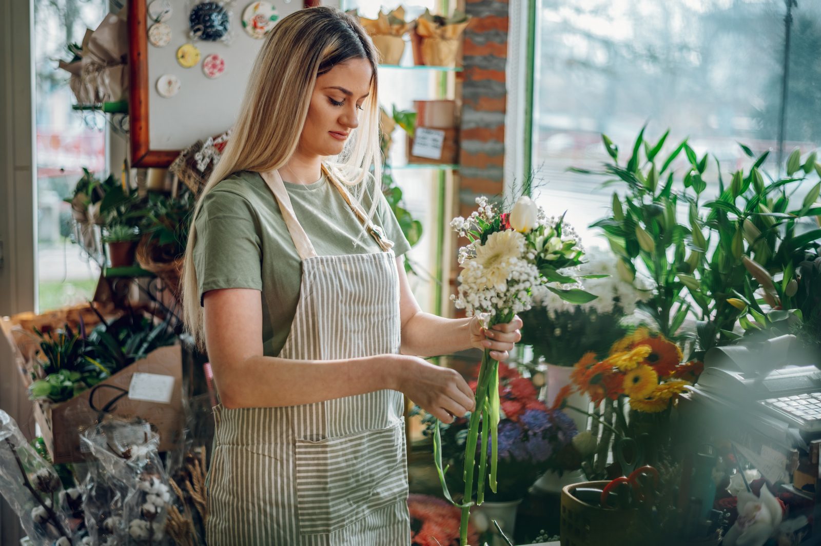 Female florist making a fresh flowers bouquet in a flower shop A florist arranging flowers behind the counter of her shop